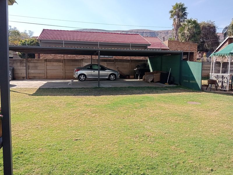 A spacious rear garden featuring a large covered carport area with concrete flooring and perimeter boundary walling.