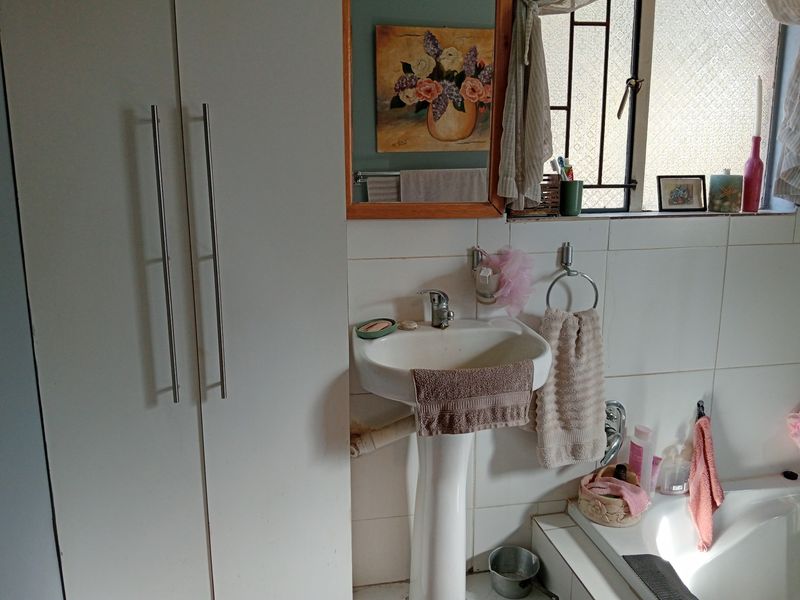A functional bathroom featuring a pedestal basin, built-in storage cupboard, and a bathtub with tiled wall finishes.