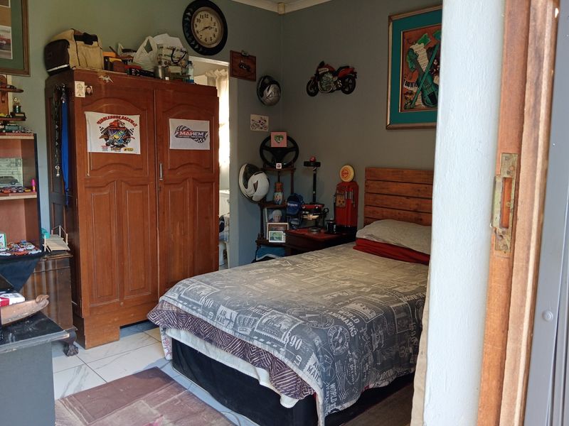 A bedroom featuring tiled flooring and a wooden door frame, currently furnished with a bed and storage unit.