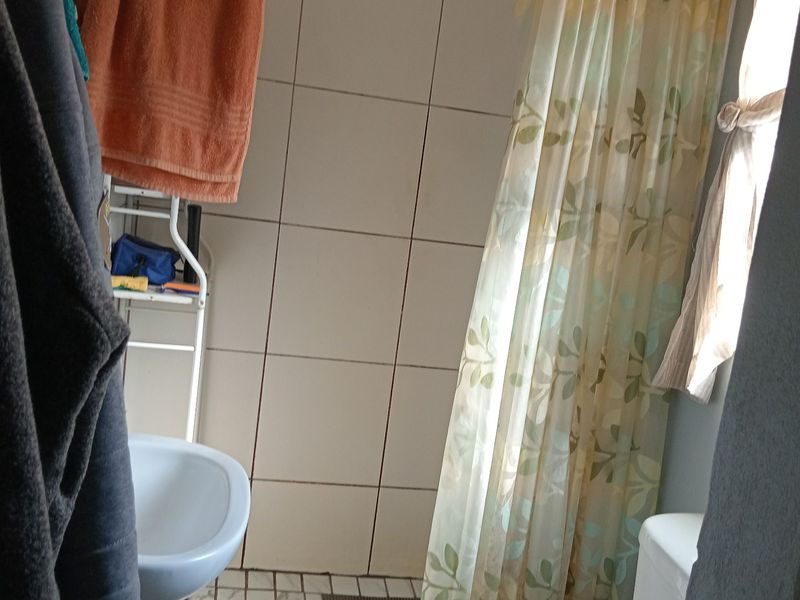 A functional bathroom featuring a shower over the basin area, tiled walls and floors, and standard sanitary ware.