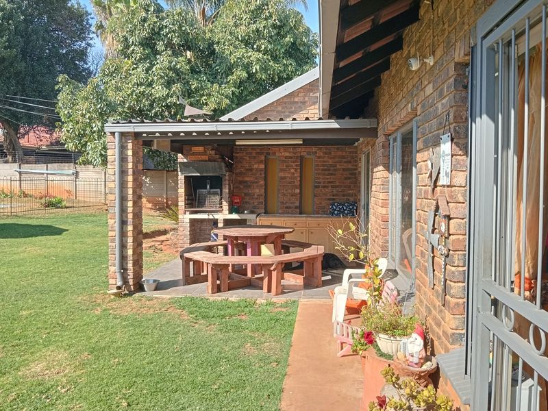 Covered outdoor patio area featuring a built-in brick braai, tiled flooring, and direct access to the rear garden.