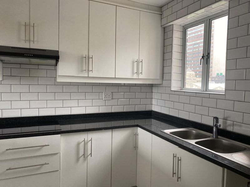 A clean, modern kitchen featuring white cabinetry, black granite countertops, subway tile backsplash, and integrated stainless steel sink and hob.