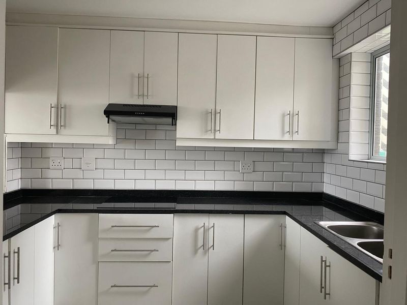 Modern kitchen featuring white cabinetry, contrasting black granite countertops, subway tile backsplash, and a stainless steel double sink.
