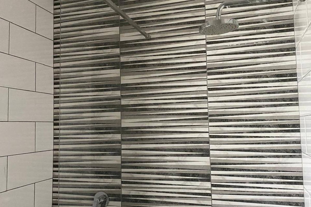 A modern shower enclosure featuring a rainfall shower head, chrome mixer, glass screen, and decorative striped accent wall tiling.
