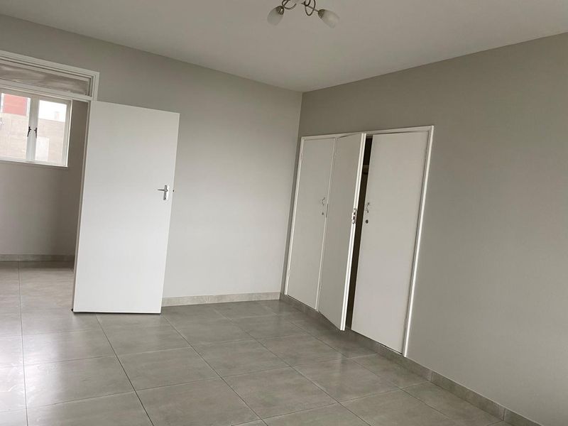 A clean, empty bedroom featuring neutral grey walls, tiled flooring, and built-in cupboards, offering a blank canvas for personalization.