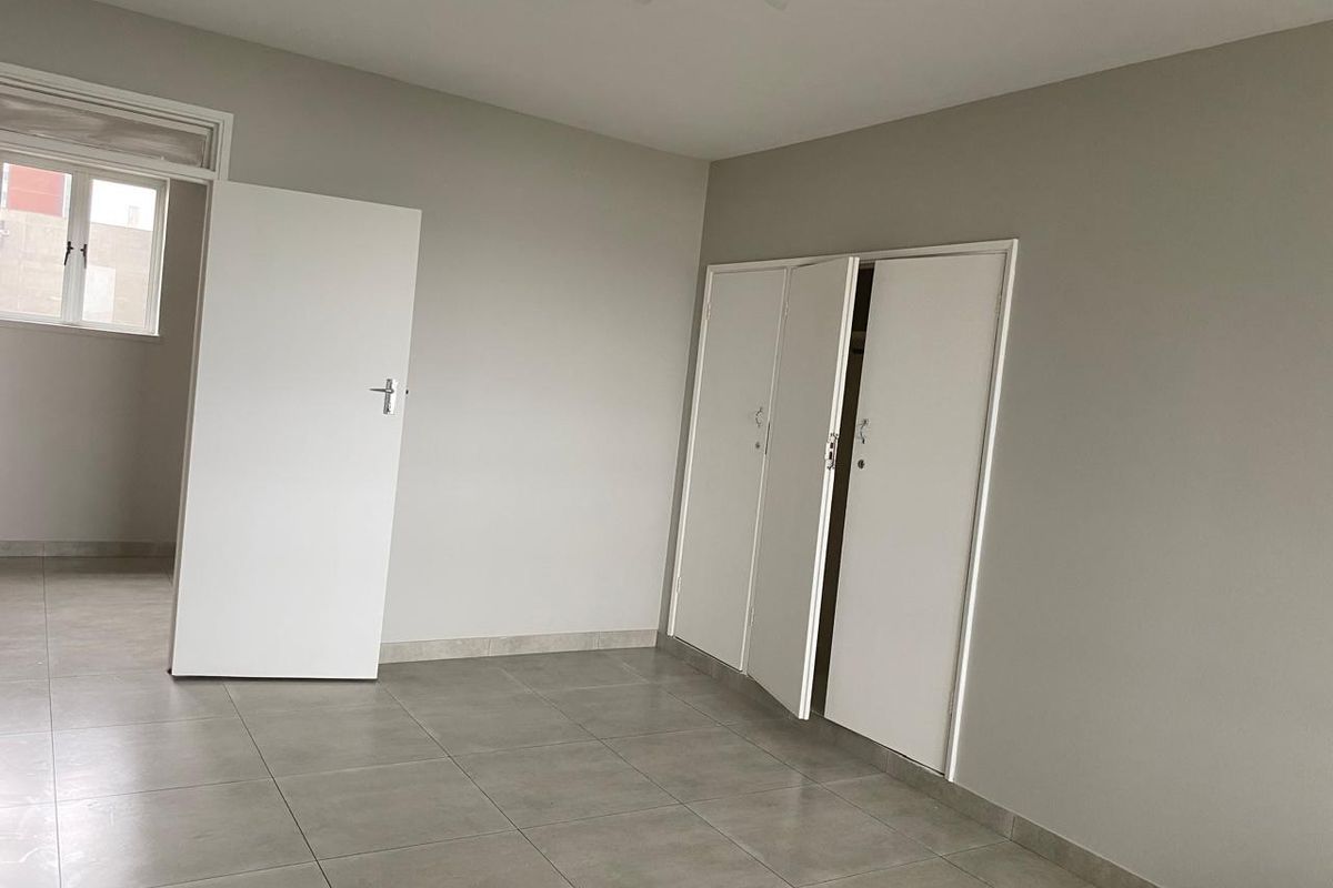 A clean, empty bedroom featuring neutral grey walls, tiled flooring, and built-in cupboards, offering a blank canvas for personalization.