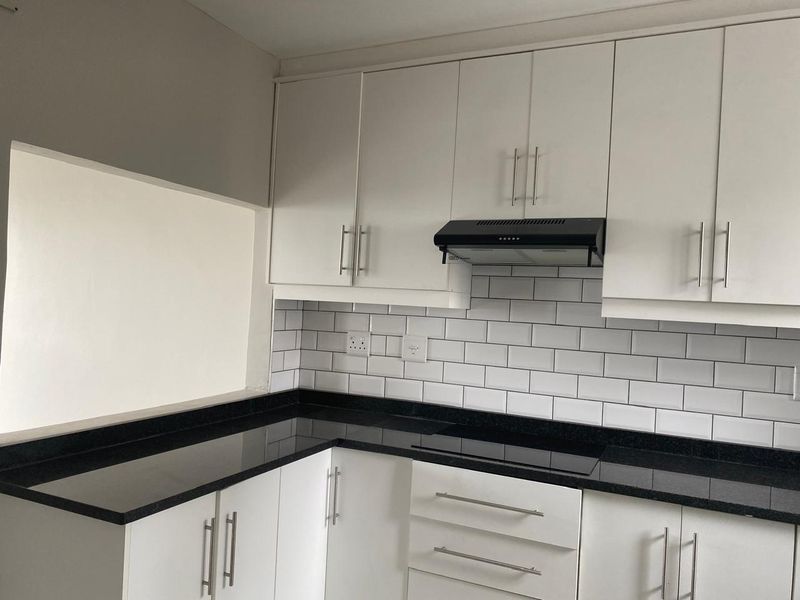 A clean, modern kitchen featuring white cabinetry, black granite countertops, and a classic subway tile backsplash with a built-in hob and extractor fan.