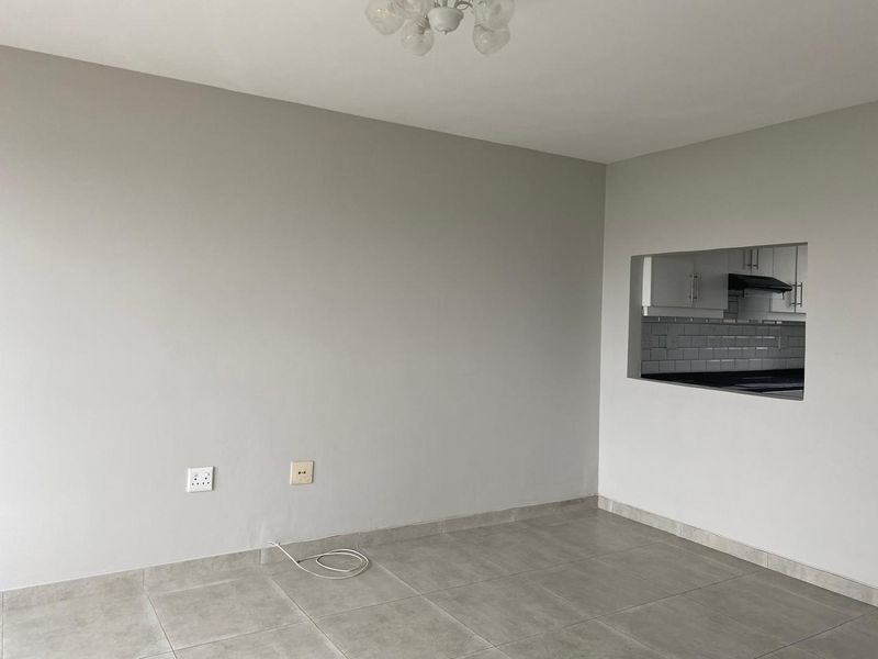 An empty open-plan living area featuring neutral tiled flooring and a convenient pass-through window connecting to the kitchen space.
