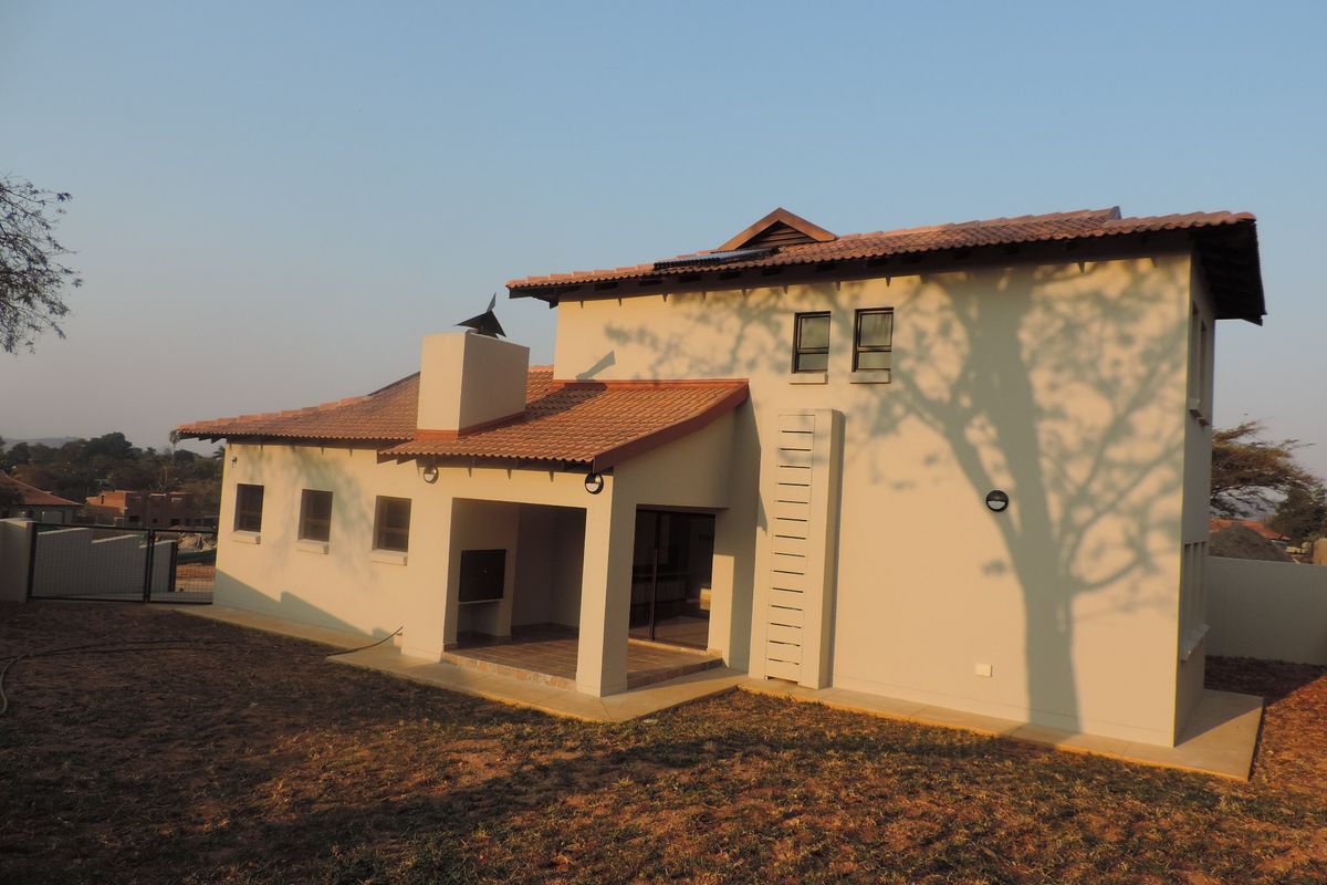 Rear view of a two-story house featuring a covered patio with a built-in braai, tiled roof, and solar water heating system.