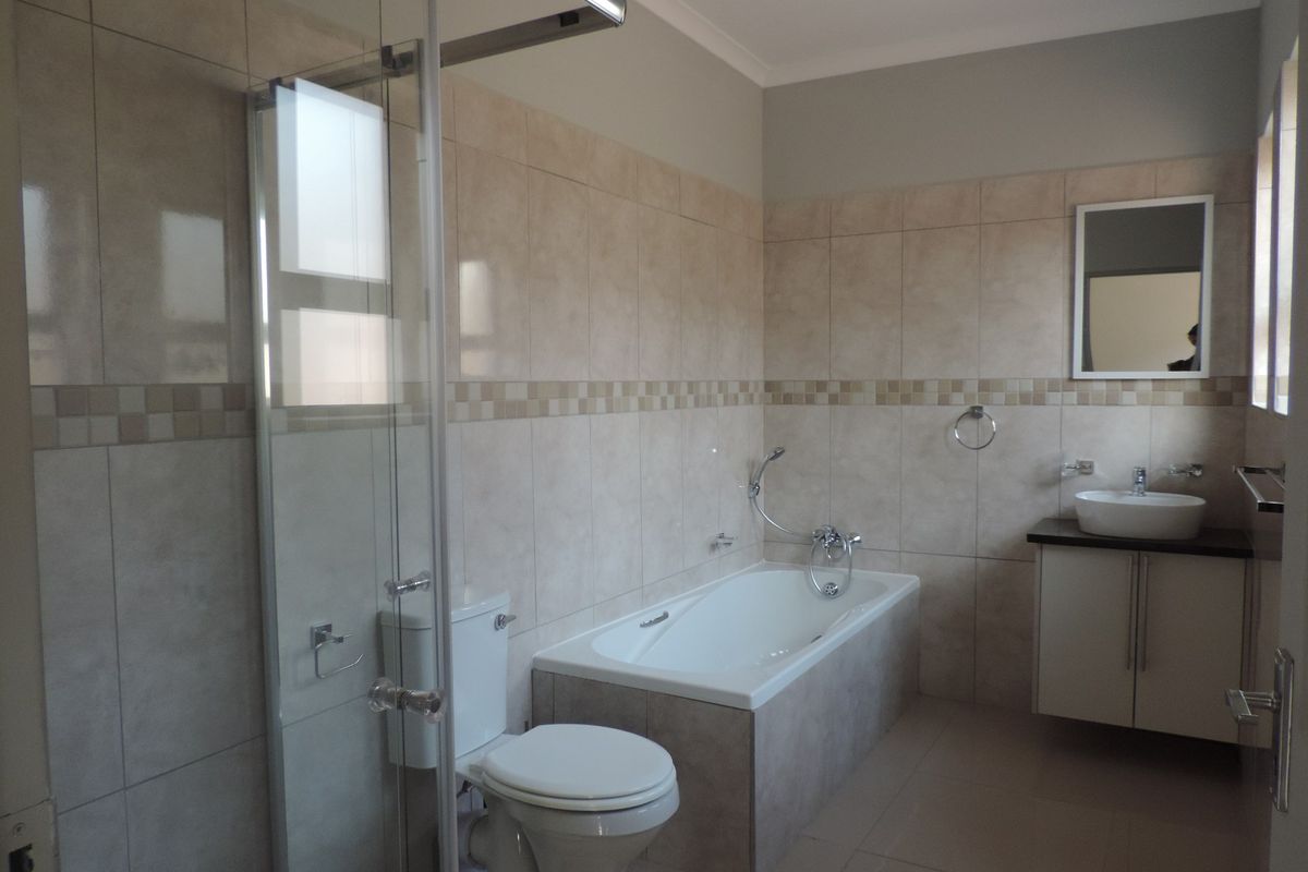A clean, modern bathroom featuring a glass shower enclosure, a built-in bathtub, a vanity with a vessel sink, and neutral wall tiling.