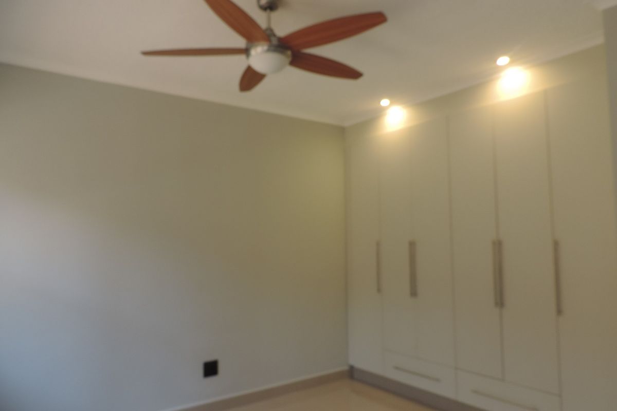 A clean, empty bedroom featuring neutral walls, built-in cupboards with modern handles, a ceiling fan, and recessed lighting.