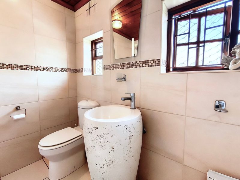 A compact bathroom featuring a unique pedestal basin, tiled walls, and a timber ceiling with natural light from the window.