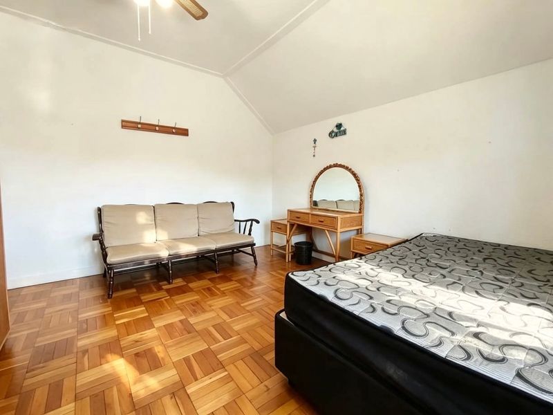 A spacious bedroom featuring polished parquet flooring, a vaulted ceiling, and a ceiling fan, offering a neutral canvas for personalization.