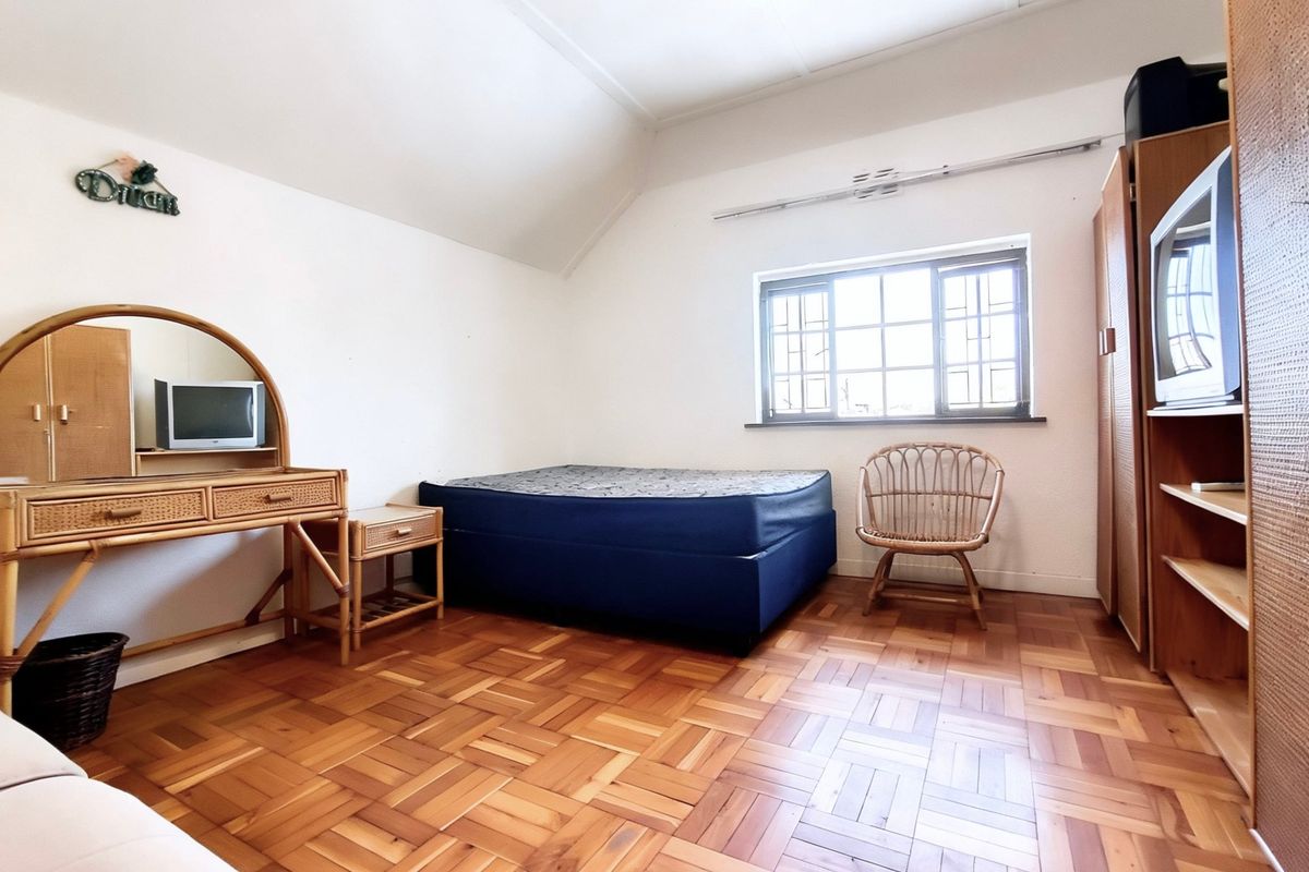 A bedroom featuring classic parquet flooring, a sloped ceiling, and a window fitted with security burglar bars.