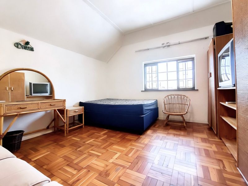 A bedroom featuring classic parquet flooring, a sloped ceiling, and a window fitted with security burglar bars.