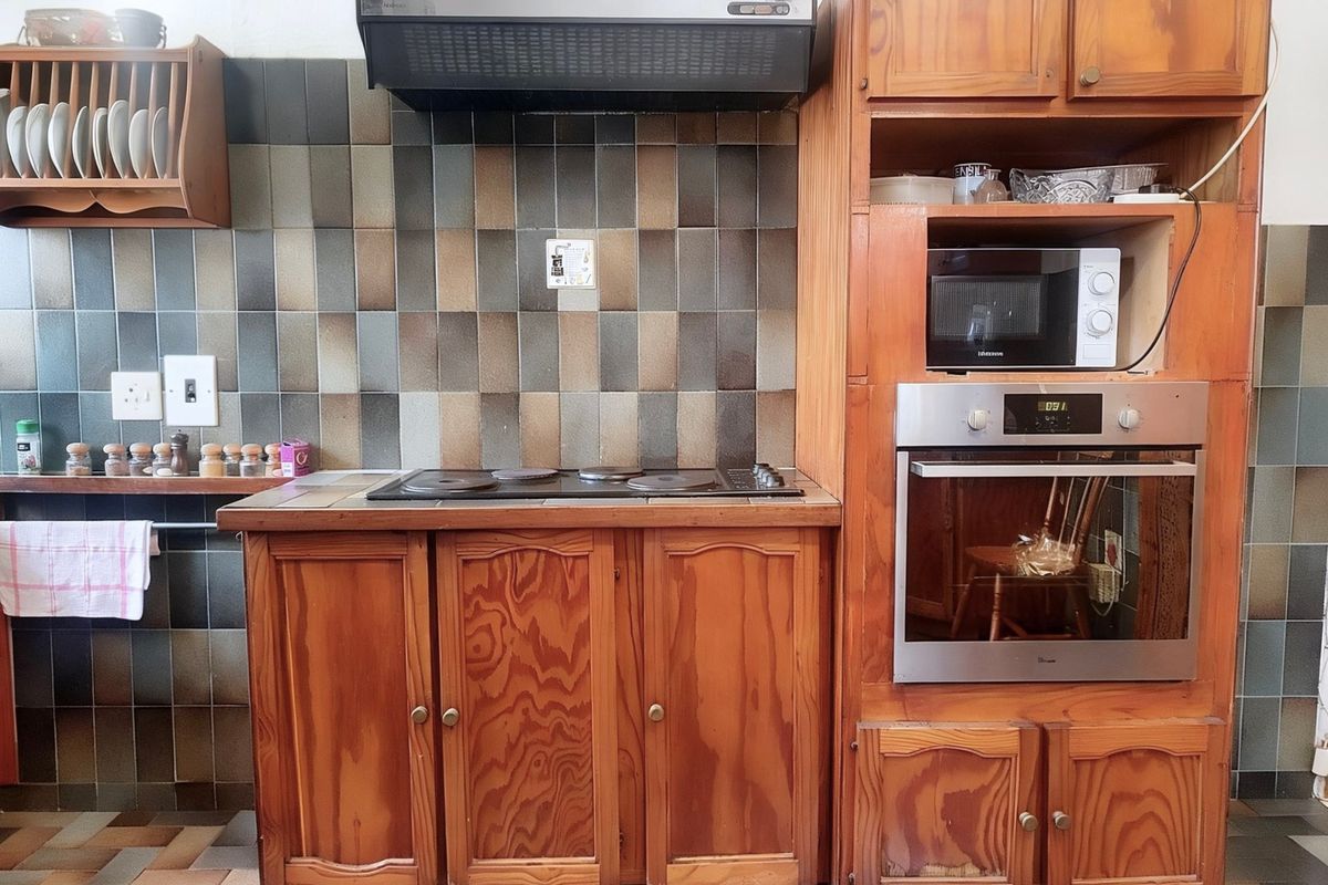 A functional kitchen featuring traditional wooden cabinetry, a built-in oven, electric hob, and a tiled backsplash.