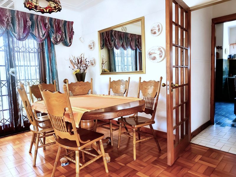 A traditional dining room featuring warm parquet flooring and a classic timber-framed glass door leading to an adjacent space.