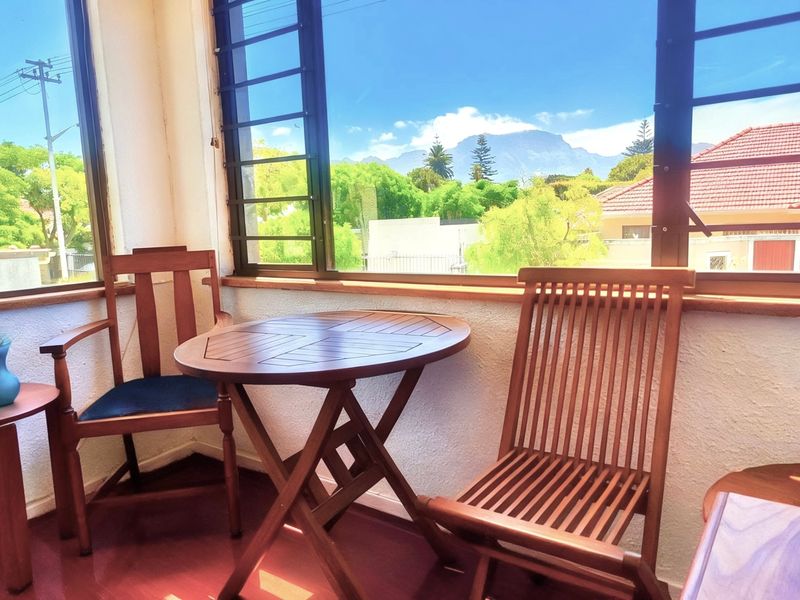 A sunlit enclosed balcony or sunroom featuring large windows with scenic mountain views and a textured wall finish.