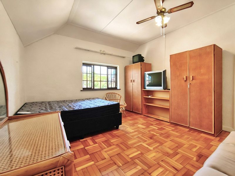 A bedroom featuring classic parquet flooring, a ceiling fan, and a casement window, offering a functional space with traditional finishes.