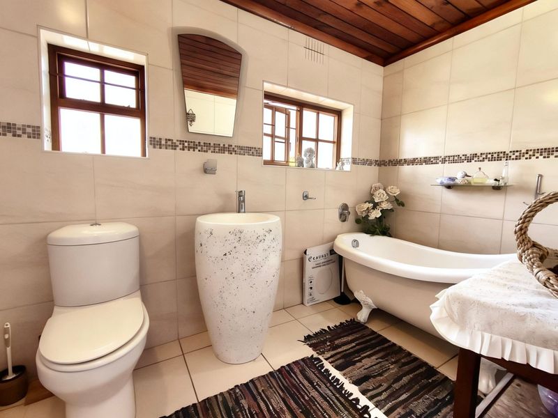 A well-maintained bathroom featuring a classic clawfoot-style freestanding bathtub, a modern pedestal basin, and a timber-paneled ceiling with tiled wall finishes.