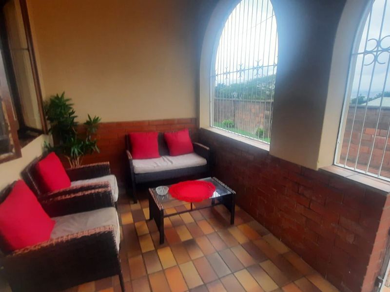 A covered patio area featuring arched windows with security bars, brick wall accents, and durable tiled flooring, offering a functional outdoor living space.