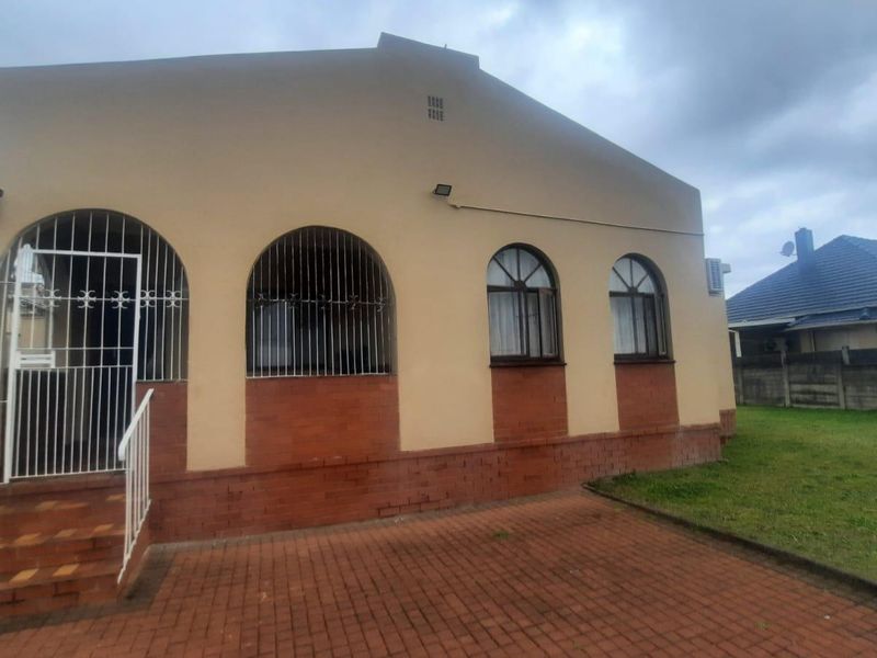 Front elevation of a house featuring arched windows with security bars, a brick base, and a paved driveway area.