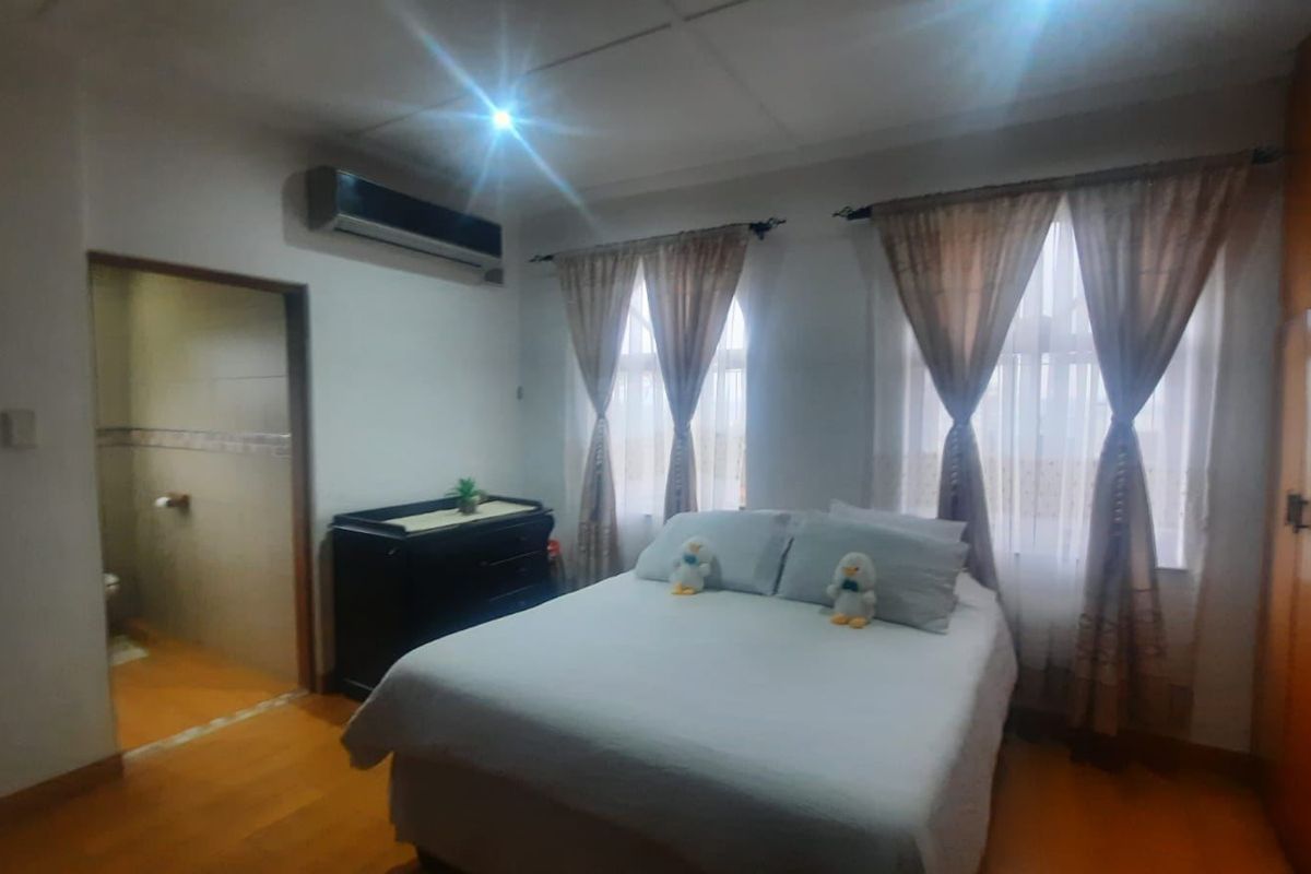 A bedroom featuring laminate flooring, a built-in wardrobe, a wall-mounted air conditioning unit, and an attached en-suite bathroom.