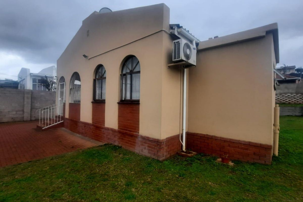 Rear exterior view of the house featuring arched windows, a brick base, and an installed air conditioning unit with a paved patio area.