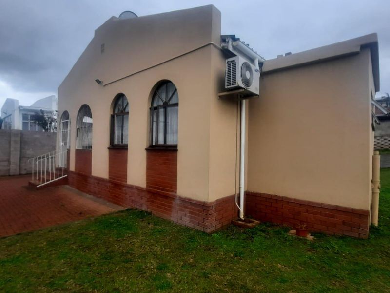 Rear exterior view of the house featuring arched windows, a brick base, and an installed air conditioning unit with a paved patio area.