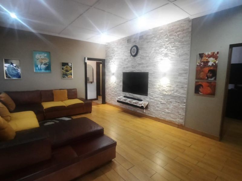 Spacious living room featuring a prominent stone-clad feature wall, warm laminate flooring, and integrated wall lighting, creating a cozy and inviting atmosphere.