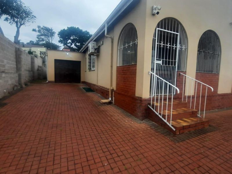 Rear exterior view of the property featuring a paved driveway, brick facade, secure arched windows, and a detached garage.
