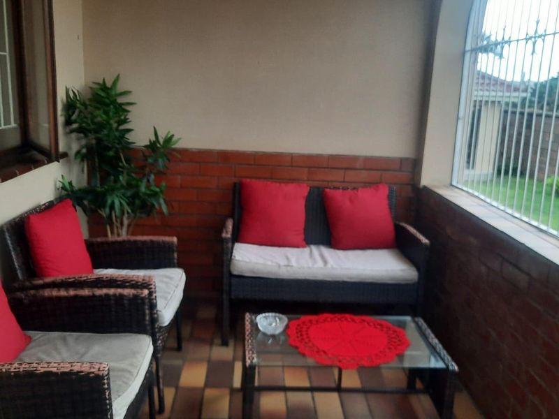 A covered patio area featuring exposed brick walls, tiled flooring, and security bars on the windows, providing a functional outdoor living space.