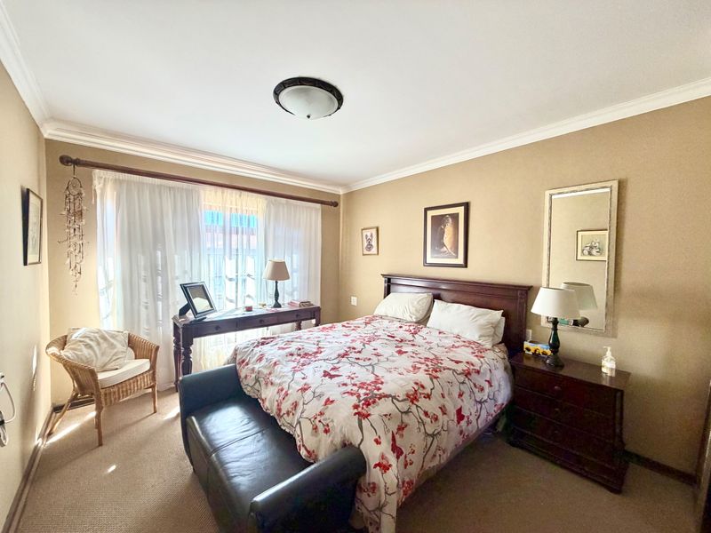 A well-lit bedroom featuring neutral wall tones, carpeted flooring, and classic ceiling cornice detailing.