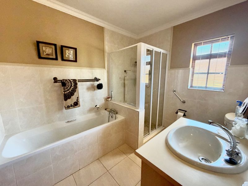 A well-maintained bathroom featuring a built-in bathtub, separate shower enclosure, and a vanity basin with tiled finishes throughout.