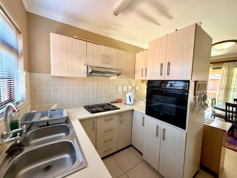 A functional kitchen featuring light wood-finish cabinetry, a built-in oven, electric hob, extractor fan, and a double bowl stainless steel sink with tiled backsplash.