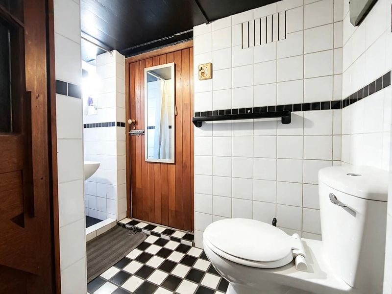 A functional bathroom featuring a classic black and white checkered tile floor, white wall tiles with a black accent border, and a wooden door.