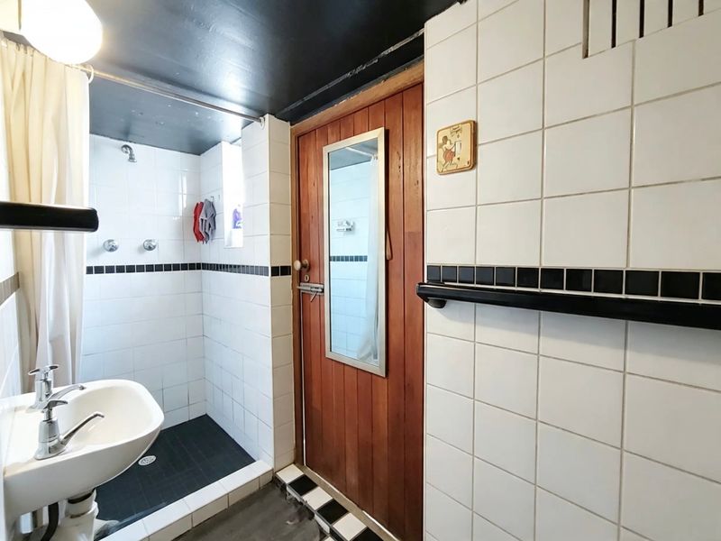 A functional bathroom featuring a pedestal basin, shower enclosure, and classic black and white tiled finishes with a timber door.