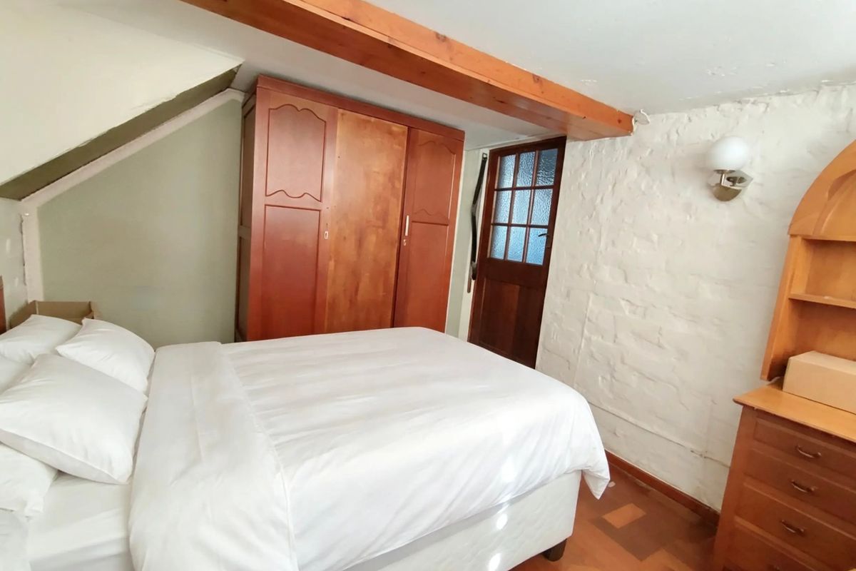 A cozy bedroom featuring an exposed timber ceiling beam, rustic exposed brick wall, and classic parquet flooring with a traditional timber door.