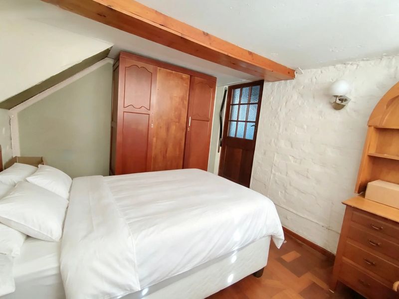 A cozy bedroom featuring an exposed timber ceiling beam, rustic exposed brick wall, and classic parquet flooring with a traditional timber door.
