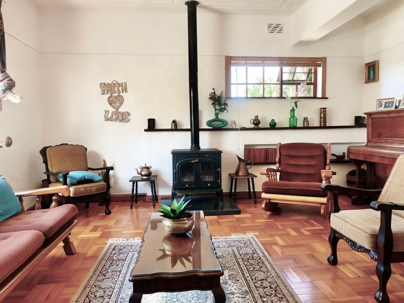A cozy living room featuring classic parquet flooring, a prominent freestanding wood-burning fireplace, and built-in wall shelving under a timber-framed window.
