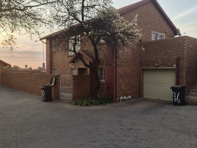 Front exterior view of a face brick townhouse featuring a paved driveway, single garage, and secure gated entrance.