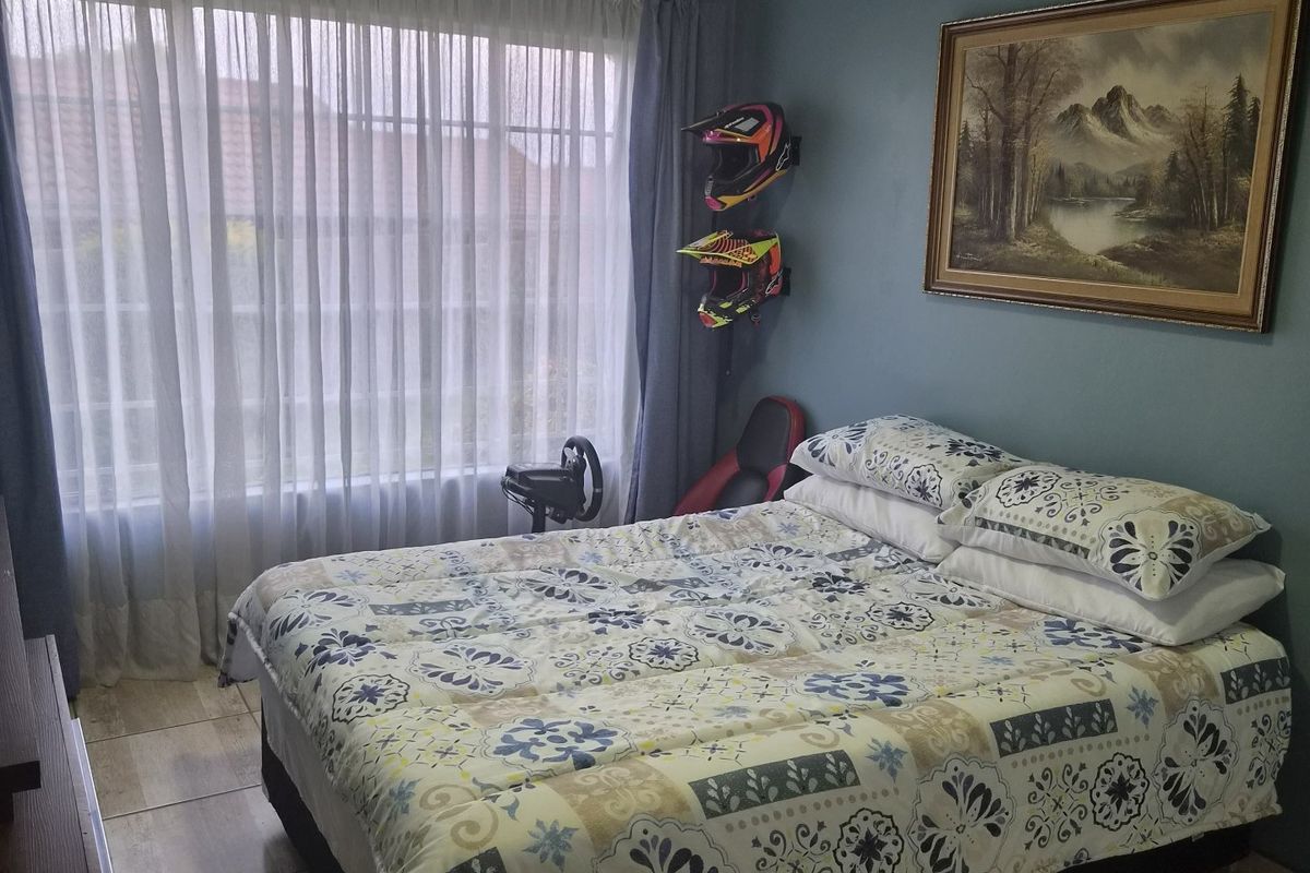 A bedroom featuring tiled flooring, blue painted walls, and a large window with curtain tracks, providing a functional and well-lit living space.