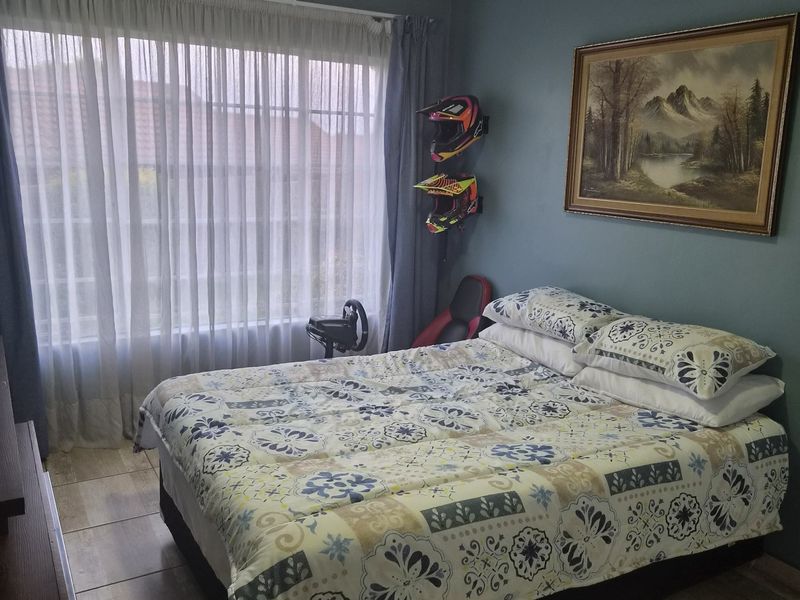 A bedroom featuring tiled flooring, blue painted walls, and a large window with curtain tracks, providing a functional and well-lit living space.