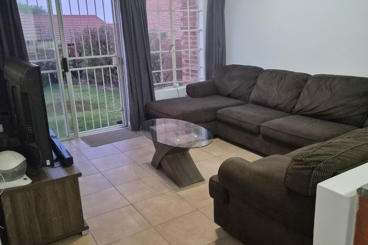A functional living room featuring tiled flooring, large windows, and a sliding glass door providing direct access to the rear garden area.