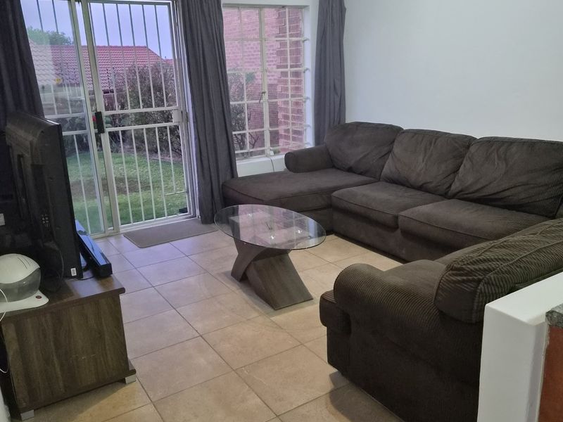 A functional living room featuring tiled flooring, large windows, and a sliding glass door providing direct access to the rear garden area.