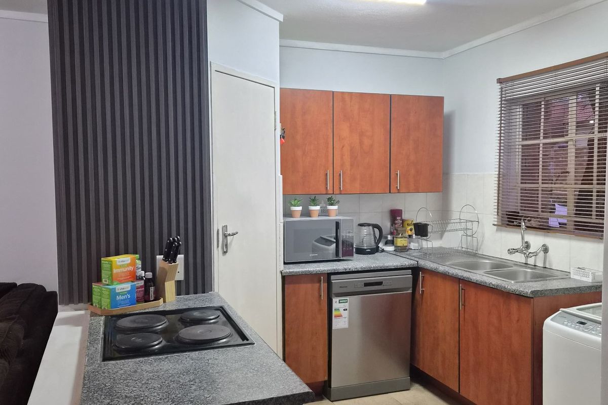 A functional kitchen featuring wood-finish cabinetry, laminate countertops, an integrated electric hob, and a double basin sink with tiled flooring.