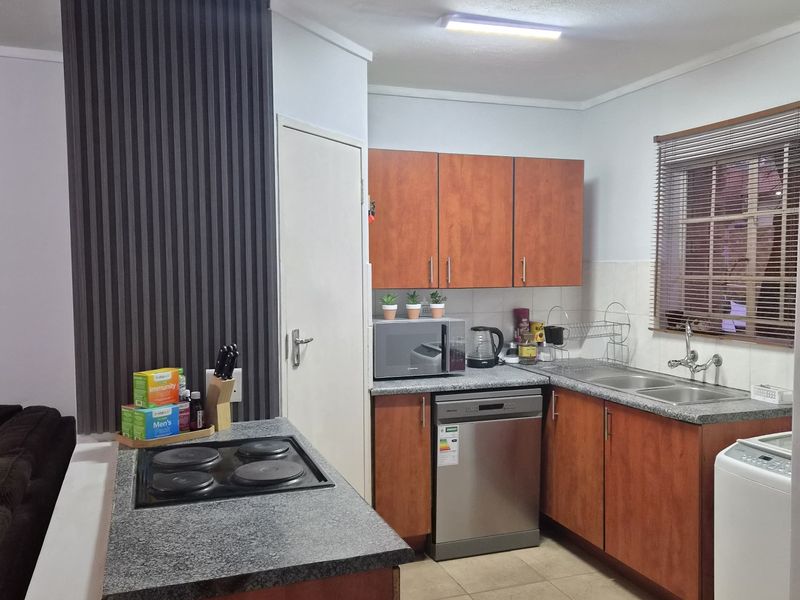A functional kitchen featuring wood-finish cabinetry, laminate countertops, an integrated electric hob, and a double basin sink with tiled flooring.