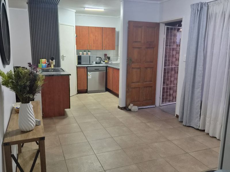 Open plan kitchen and living area featuring tiled flooring, wooden cabinetry, and direct access to an exterior security gate.
