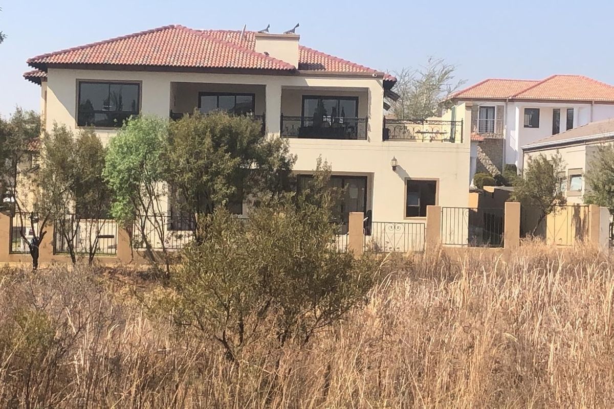 Rear view of a two-story residential house featuring a terracotta tile roof, upper-level balcony with wrought iron railings, and a perimeter wall.