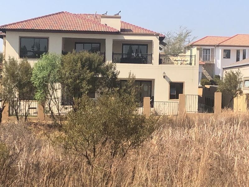 Rear view of a two-story residential house featuring a terracotta tile roof, upper-level balcony with wrought iron railings, and a perimeter wall.